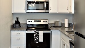 Une cuisine de taille réduite avec des meubles blancs, un four à micro-ondes en acier inoxydable, une cuisinière et un réfrigérateur.