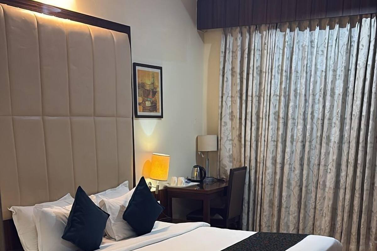 Ett hotellrum med en stor säng, ett skrivbord, en stol, en lampa och en tavla på väggen.