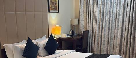 A hotel room with a large bed, a desk, a chair, a lamp, and a painting on the wall.