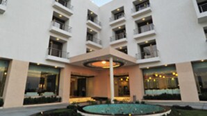A modern hotel with a central courtyard, multiple balconies, and a well-lit entrance. - KRSNA Lila By The Blues Hotels (Sanand)