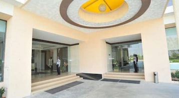 A modern building entrance with glass doors, a security guard, and a yellow circular design on the ceiling.
