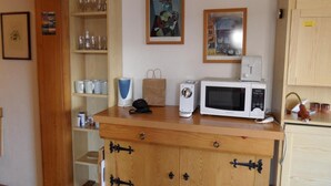 A kitchen with wooden cabinets, a microwave, a toaster, and a coffee maker. There are shelves with glassware and a framed picture on the wall.