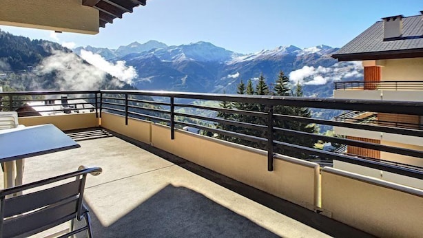 A balcony with a view of snow-capped mountains, a table, and chairs.