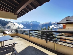 Un balcón con vistas a montañas nevadas, una mesa y sillas.