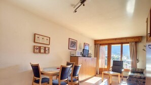 A dining area with a round table and six chairs, a kitchenette with a microwave, and a view of the city through large windows. - Studio *** - 6th floor - close to the centre, shops and bus stop - sunny balcony with very nice view (Verbier)