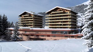 A multi-story hotel with balconies, situated in a snowy landscape with mountains in the background. - Studio *** - 6th floor - close to the centre, shops and bus stop - sunny balcony with very nice view (Verbier)