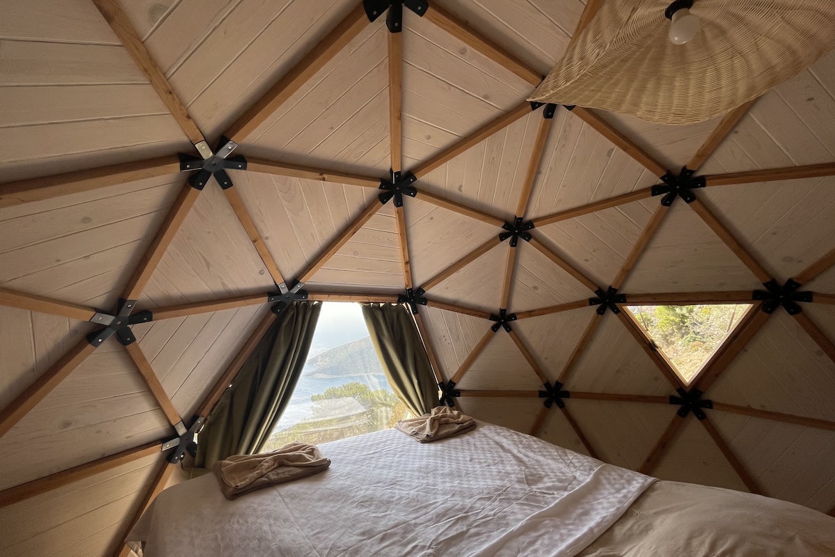 Une pièce triangulaire comprenant un lit, une fenêtre et un luminaire suspendu.