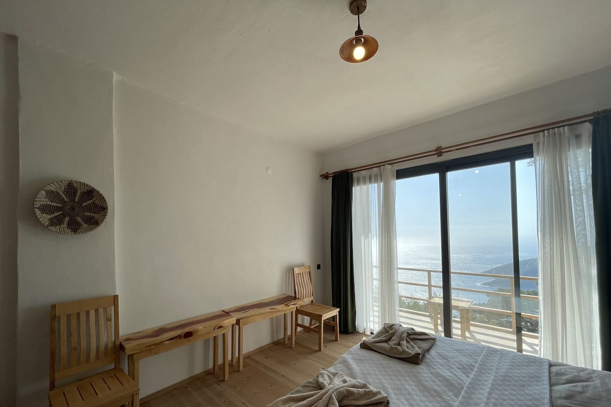 Une chambre dotée d’un grand lit, d’un bureau, d’une chaise et offrant une vue sur la mer grâce à de grandes fenêtres.