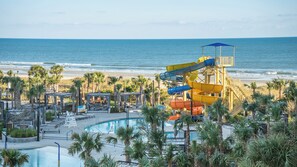 A water park with a large pool, palm trees, and a beach view.