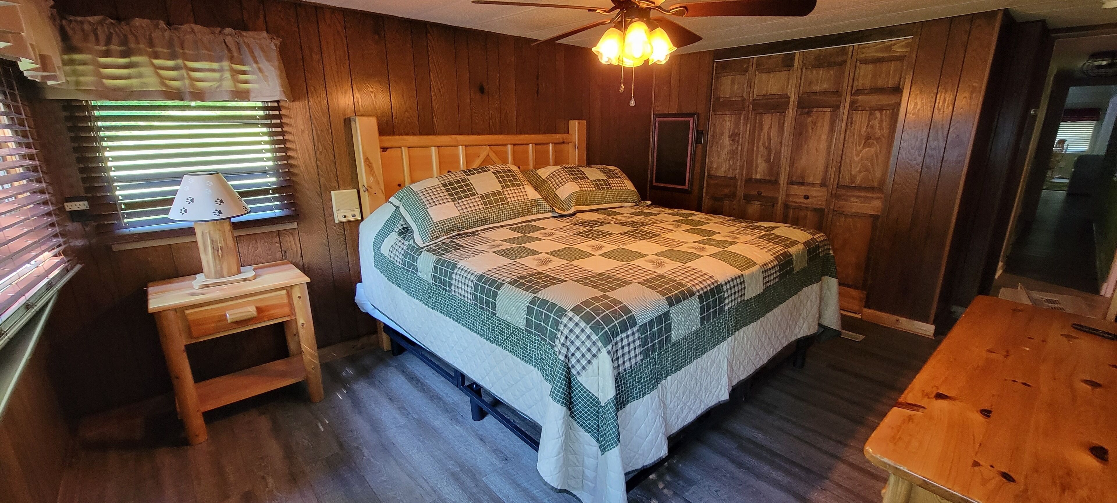 A wooden-paneled bedroom with a bed, a nightstand, a lamp, and a ceiling fan.