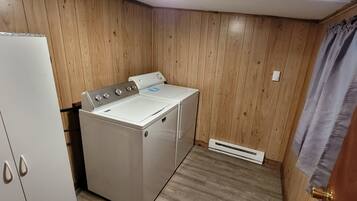 A laundry room with a white washer and dryer, wooden walls, a white cabinet, and a vent.