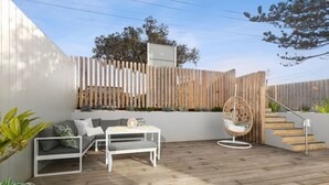 Una terraza de madera con un sofá blanco, una mesita y una silla colgante.