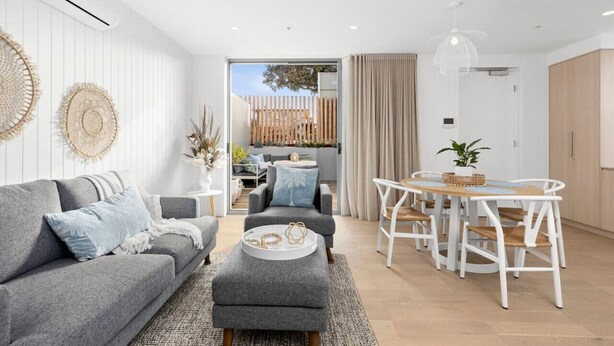 Una sala de estar moderna con un sofá gris, una mesa de centro redonda y una zona de comedor con una mesa y sillas blancas.