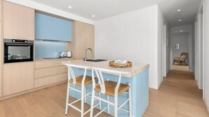 Una cocina moderna con una isla central, taburetes blancos y un lavamanos visible.