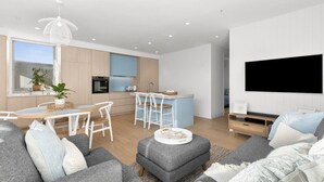 Una sala moderna con un sofá gris, un reposapiés y un comedor con una mesa y sillas blancas.