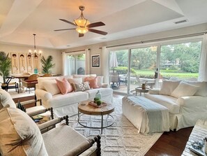 A spacious living room with a ceiling fan, large windows, and a view of the outdoors.