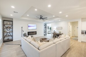 A modern living room with a sectional sofa, a coffee table, and a TV. There is a bookshelf and a dining area visible in the background. - 3 King En Suites - Single-Level, Walk to Clubhouse (Saint George)