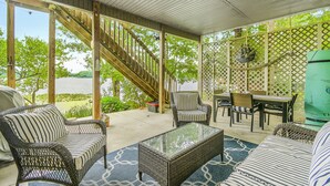 A covered patio with wicker furniture, a glass coffee table, and a staircase leading to a deck.