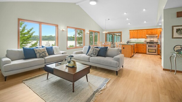 A spacious living room with a large sofa set, a coffee table, and a view of a kitchen with wooden cabinets and a large window.