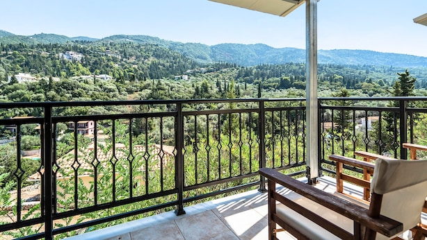 Un balcone con vista su un paesaggio montuoso, una panca di legno e una ringhiera in metallo.