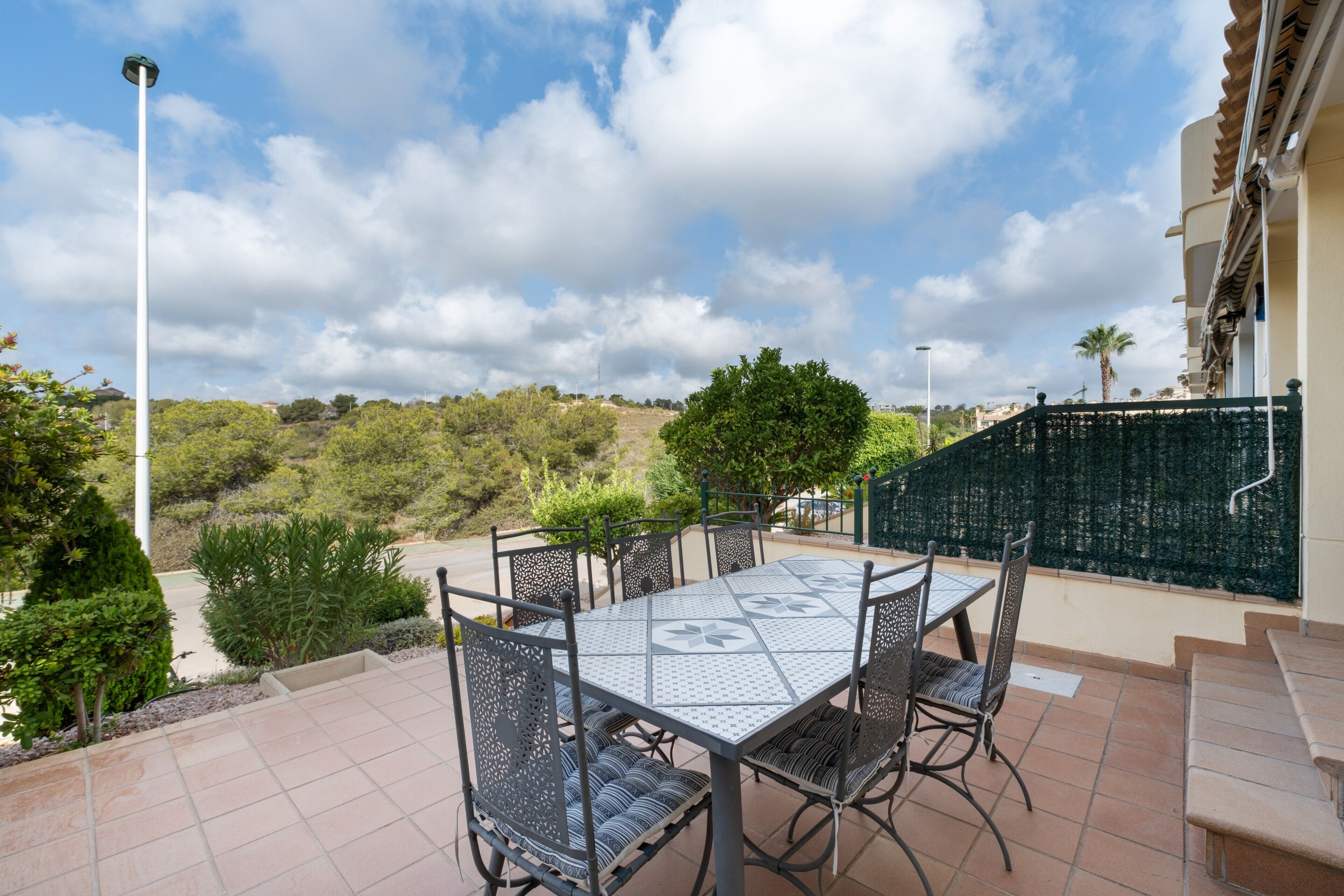 Un patio exterior con una mesa y sillas, rodeado de vegetación y vistas del paisaje.