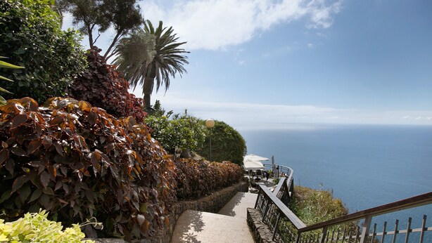 Un camí costaner amb mur de pedra, vegetació i vista al mar.