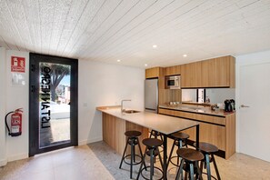 A modern kitchen with a central island, bar stools, wooden cabinets, a stainless steel refrigerator, and a microwave.