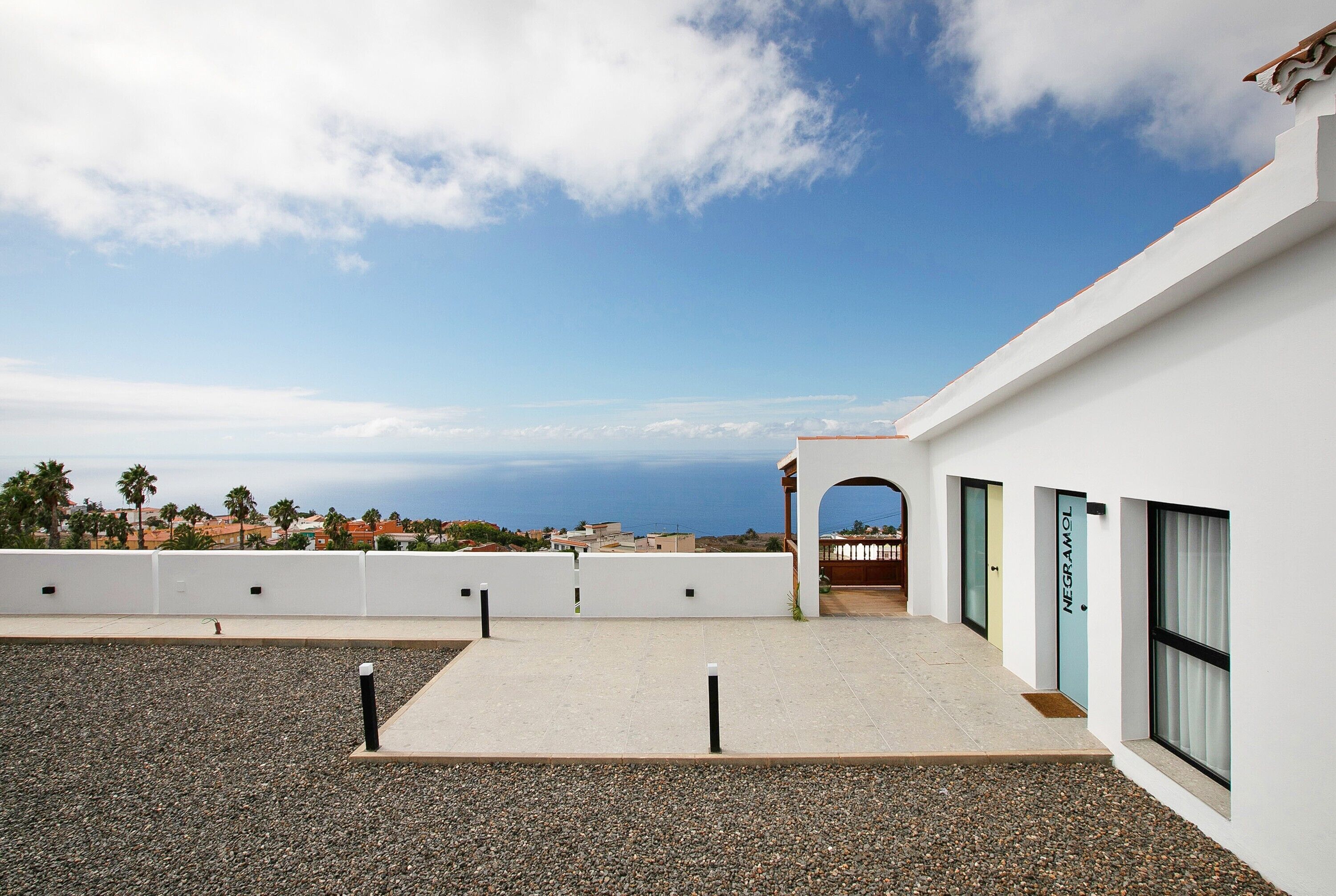 Una terraza en la azotea con vistas despejadas al mar, un edificio blanco de diseño moderno y una puerta con la leyenda 'NEGRAMOL'.