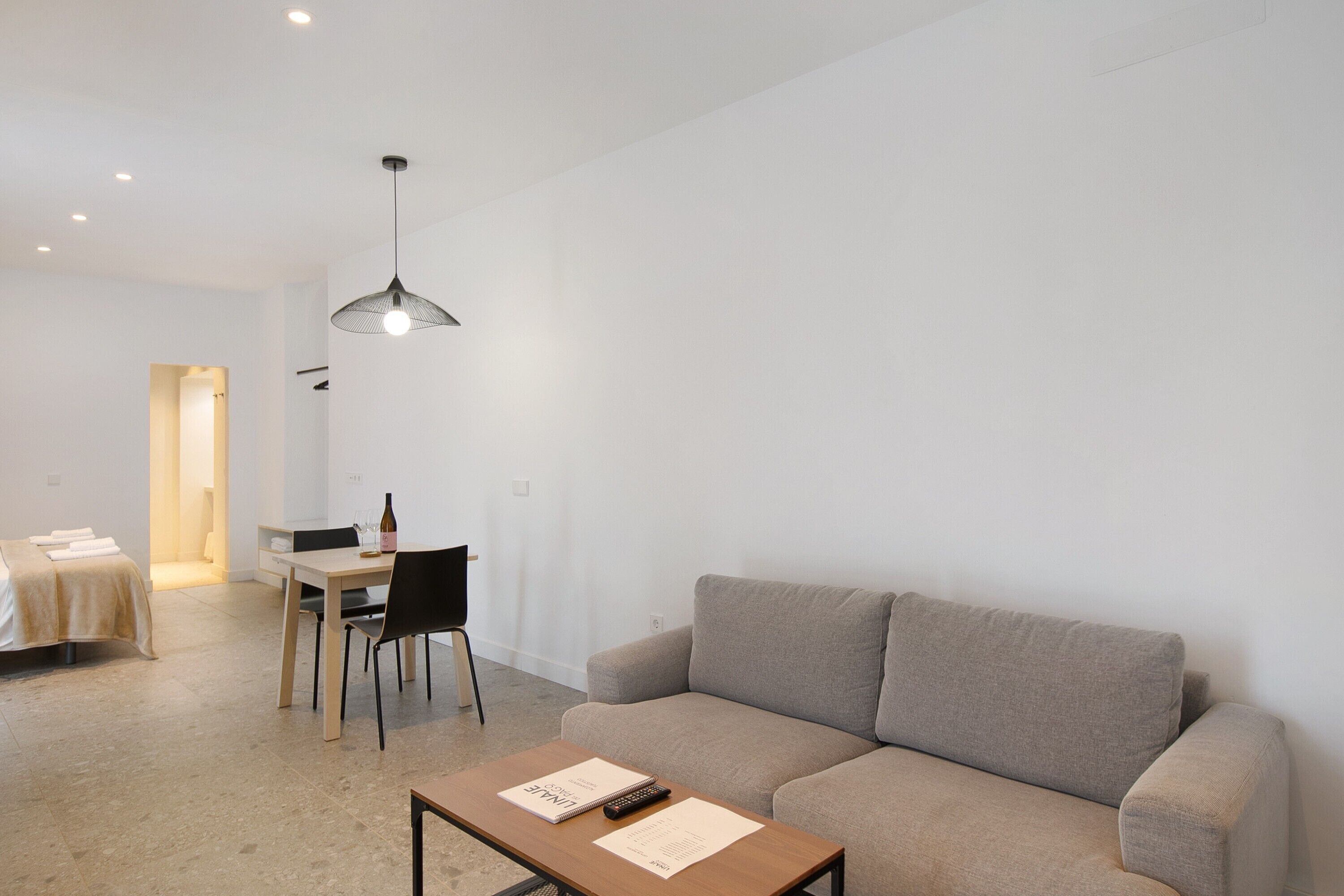 A modern, minimalistic living room with a sofa, a dining table, and a pendant light.