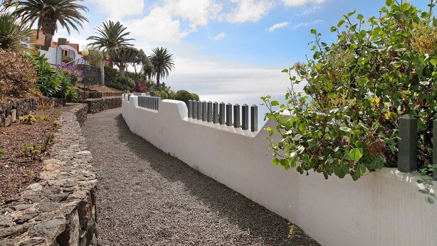 A pathway leading to a building with a white wall and a stone border, surrounded by greenery and palm trees. - Vacation Home 'Linaje del Pago Negramol' with Sea View, Pool & Wi-Fi (Sauzal)