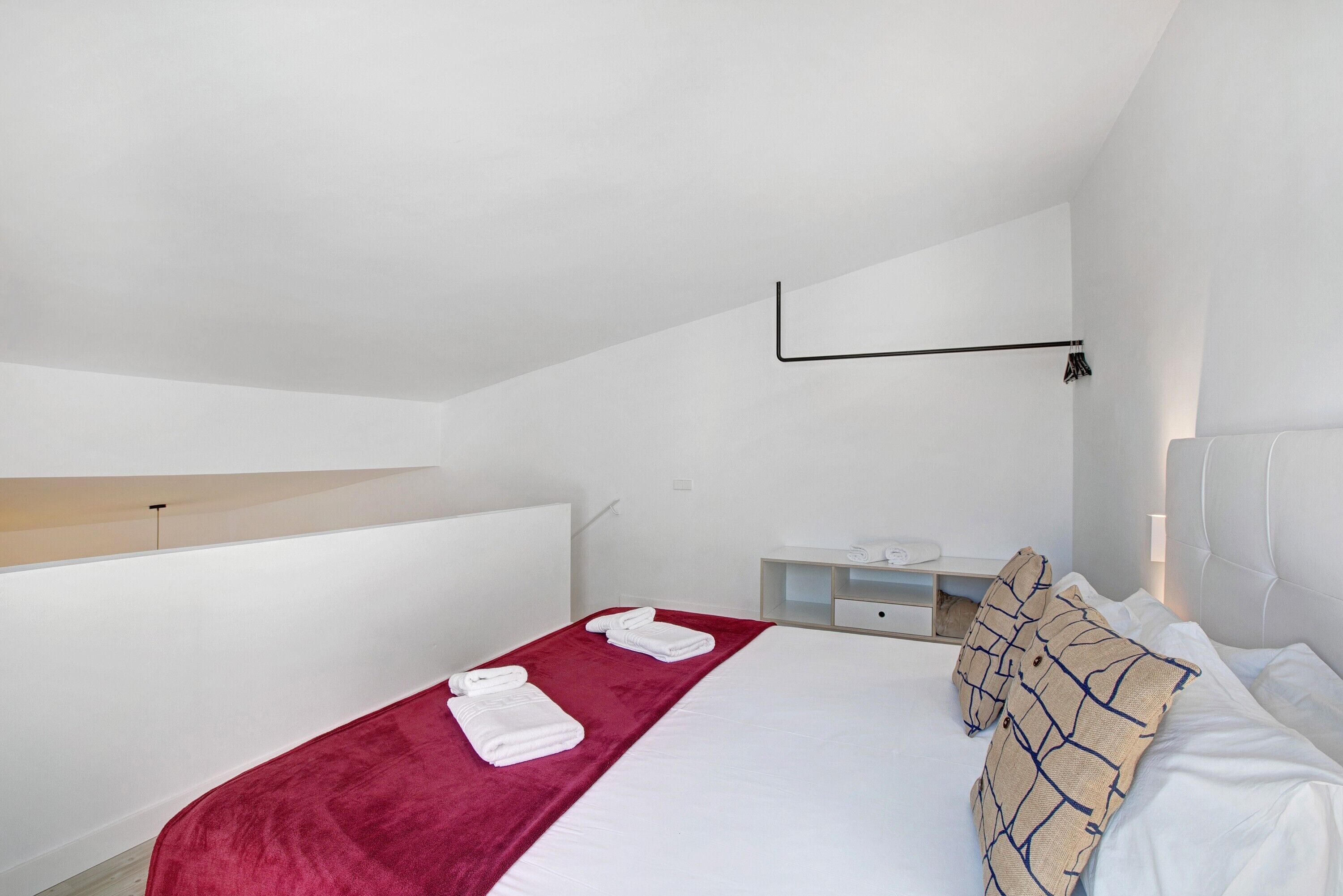 Ein Hotelzimmer mit einem Bett, einer roten Decke, weißen Kissen, einem Holzbodenregal, einem Nachttisch und einer Wandleuchte.