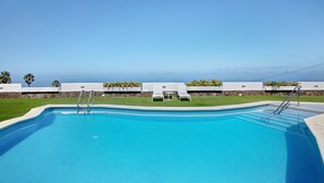 A clear blue swimming pool with lounge chairs and a table, surrounded by a white wall and a stone retaining wall. - Vacation Home 'Linaje del Pago Negramol' with Sea View, Pool & Wi-Fi (Sauzal)