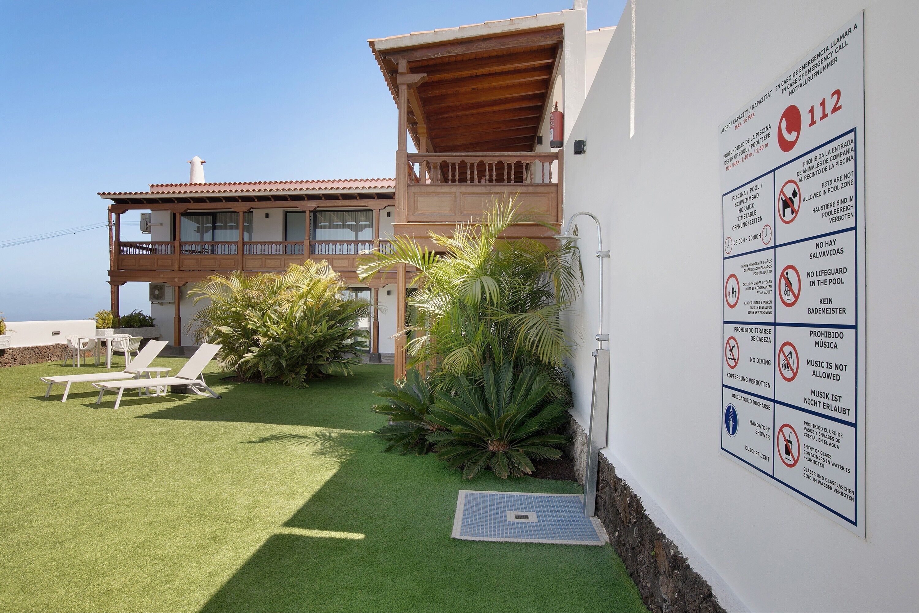 A two-story building with a balcony, a pool area, and a sign with various prohibitions and emergency contact information.