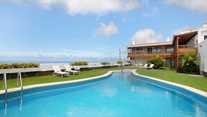 Una piscina con sillones de descanso, vista al océano y un edificio con balcón.