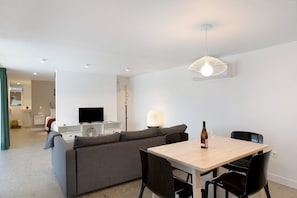 A modern living room with a sofa, a dining table with chairs, a TV, and a pendant light.