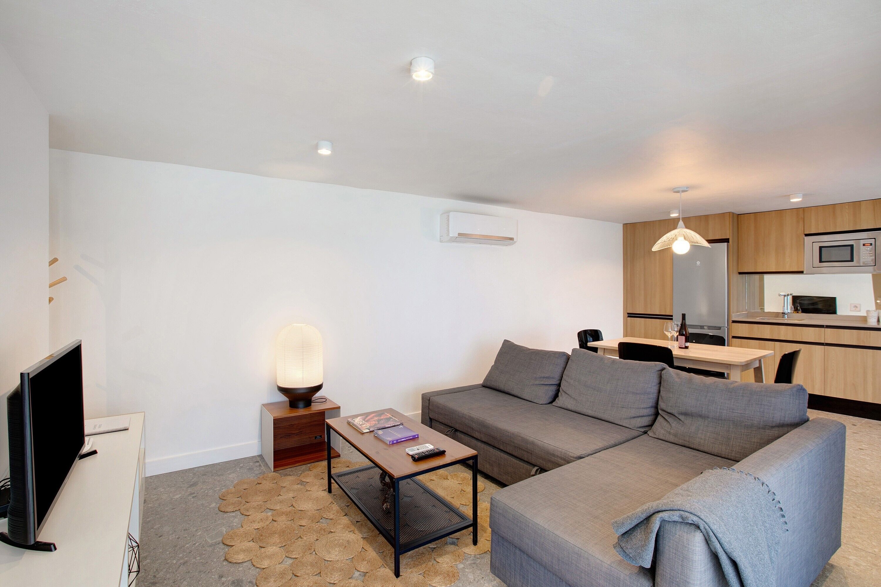 A modern living room with a sofa, coffee table, TV, and a small dining area with a table and chairs.