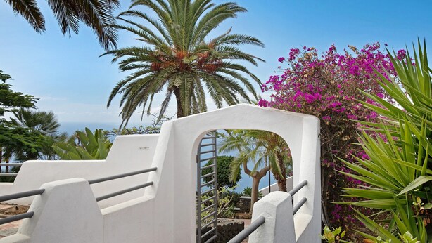 A white concrete structure with metal railings, surrounded by lush greenery and a view of the sea. - Vacation Home 'Linaje del Pago Malvasia' with Sea View, Pool, Private Balcony & Wi-Fi (Sauzal)