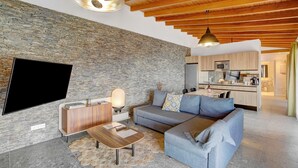 A modern living room with a stone wall, wooden ceiling, and a flat-screen TV. - Vacation Home 'Linaje del Pago Malvasia' with Sea View, Pool, Private Balcony & Wi-Fi (Sauzal)