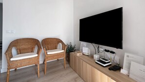 Een kamer met twee rieten stoelen, een flatscreen televisie, een houten dressoir en een plant.