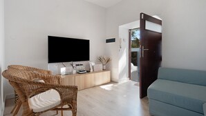 Een moderne woonkamer met een flatscreen televisie, rieten stoelen, een lichtblauwe bank en een houten kast.