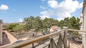 Un balcón con vistas a una calle, árboles y coches aparcados.