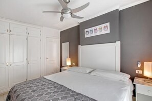 Une chambre d’hôtel comprenant un lit, un ventilateur de plafond, une table de chevet avec une lampe, une horloge murale et une armoire.