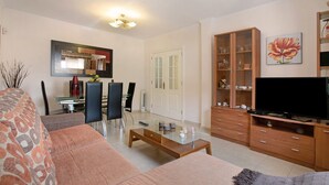 Una sala de estar con sofá, mesa de centro, mueble para televisión y un comedor con sillas y mesa.