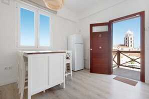 Une pièce avec une porte à cadre en bois, un réfrigérateur blanc, un meuble blanc et une fenêtre donnant sur une tour.