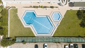 Eine Vogelperspektive auf ein Hotel mit einem großen zentralen Schwimmbecken, einem kleineren Pool und einem überdachten Außenbereich mit Sitzgelegenheiten.