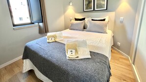 Ein ordentlich eingerichtetes Schlafzimmer mit einem Bett, Kissen, einem Nachttisch, einem Fenster mit Vorhängen und Wandleuchten.