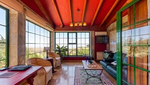 Una habitació àmplia amb grans finestres, sostre vermell i una porta de vidre amb marc verd.