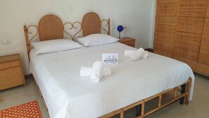 A neatly made bed with white linens and two rolled towels, a wooden nightstand with a lamp, and a wardrobe in a room with a simple, clean design. - Mini apartment "CirPi" (max 4 people) Desusino near the sea (Butera)