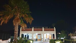 A two-story building with a balcony, a palm tree in the foreground, and a view of the night sky. - Mini apartment "CirPi" (max 4 people) Desusino near the sea (Butera)