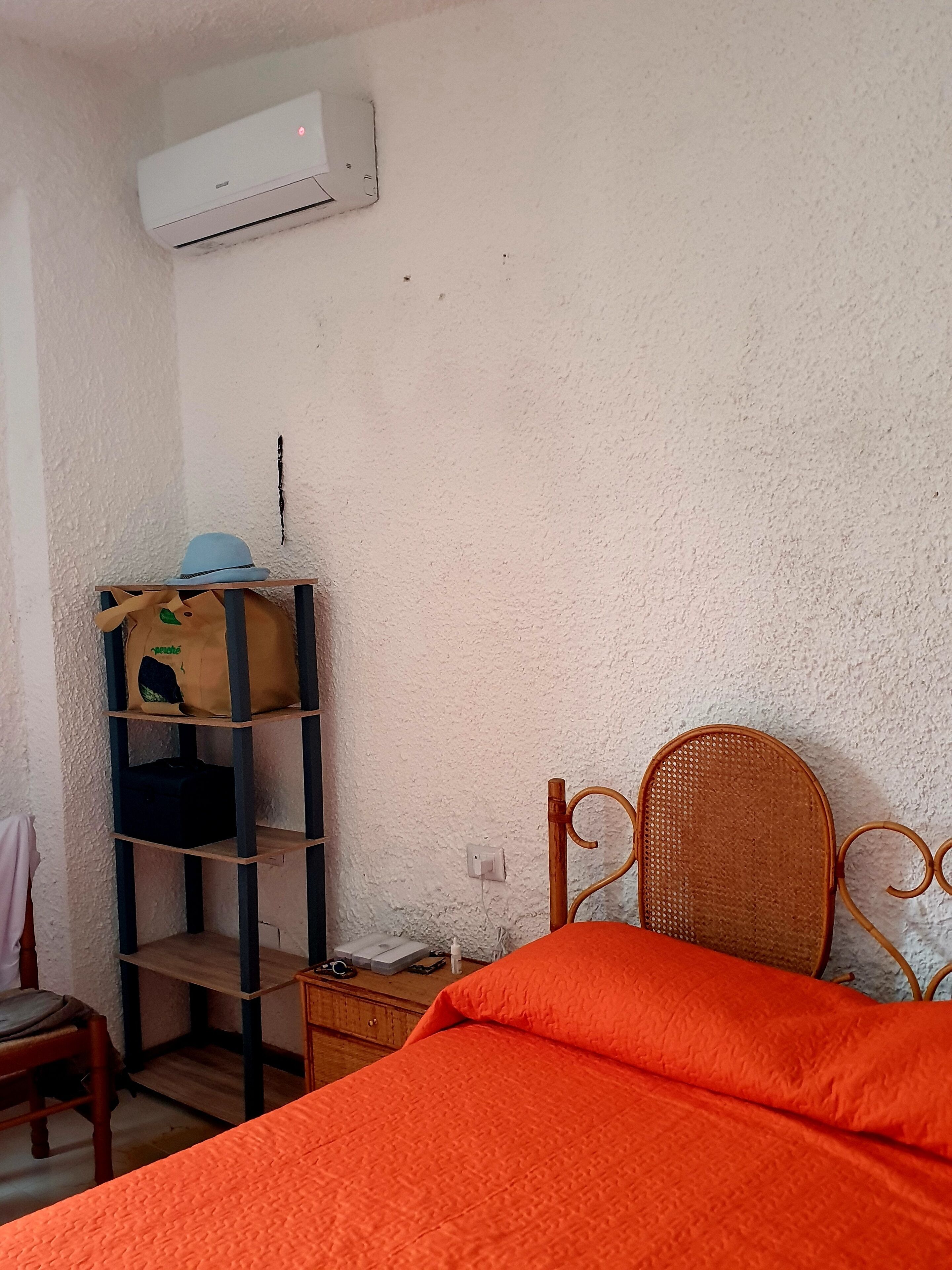 Una camera da letto con un letto, uno scaffale con una borsa, una sedia e un condizionatore d'aria.